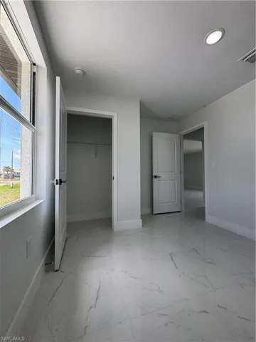 Unfurnished bedroom with a textured ceiling, light marble finish floors, and a walk in closet