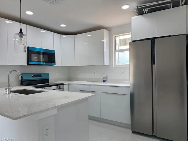 Kitchen featuring freestanding refrigerator, electric range, light stone counters, modern cabinets, and white cabinetry