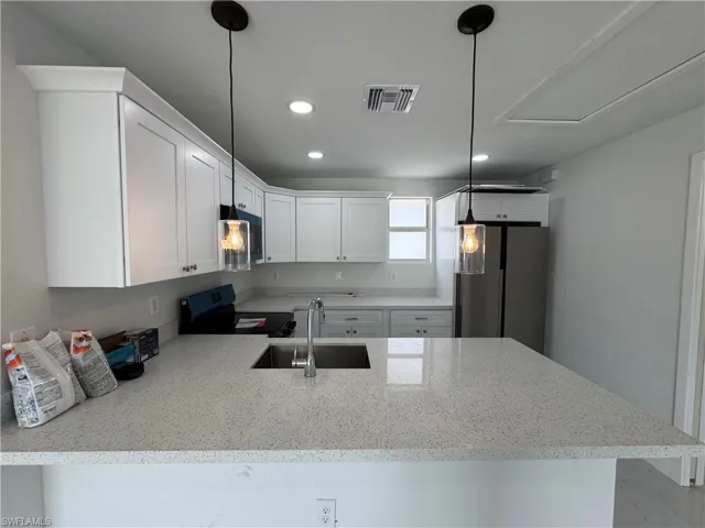 Kitchen with a peninsula, white cabinetry, stainless steel appliances, light stone counters, and pendant lighting