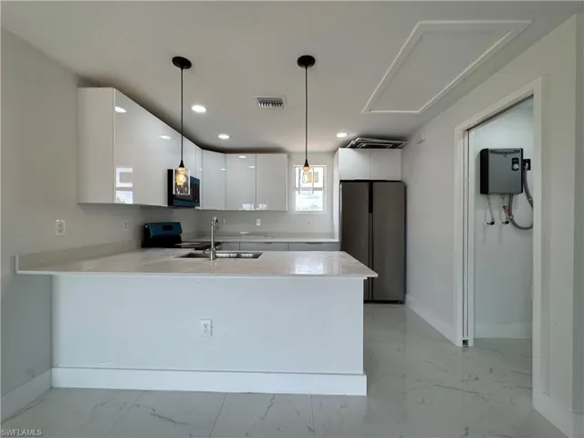 Kitchen with light stone countertops, white cabinets, freestanding refrigerator, a peninsula, and light marble finish floors