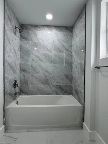 Bathroom featuring light marble finish flooring and tub / shower combination