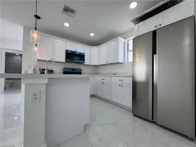 Kitchen with stainless steel fridge, light marble finish flooring, white cabinetry, decorative light fixtures, and range