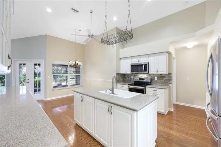 Kitchen with stainless steel appliances, backsplash, white cabinetry and island