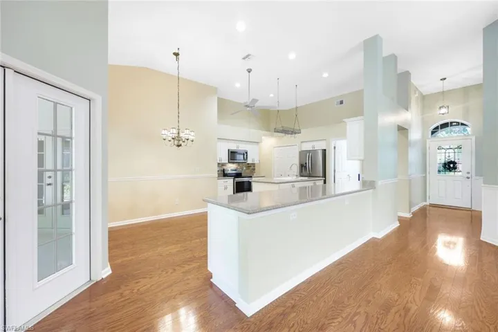 Kitchen with hardwood flooring throughout, hanging light fixtures, white cabinetry, and high vaulted ceiling
