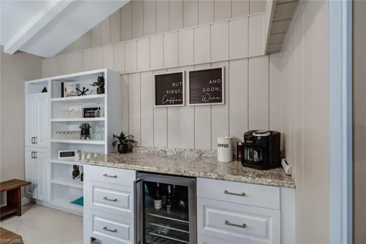 Indoor dry bar with wine cooler, light marble finish flooring, and lofted ceiling