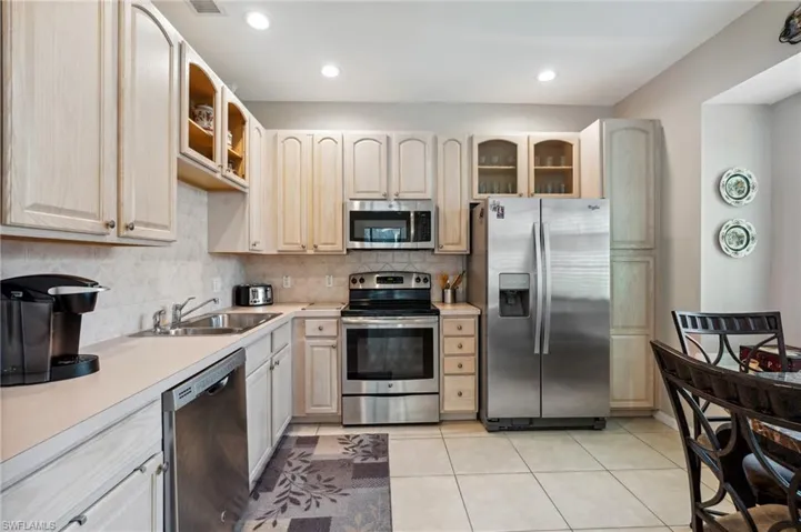 Kitchen with decorative backsplash, appliances with stainless steel finishes, light tile patterned flooring, and sink
