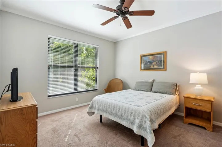 Carpeted bedroom with ceiling fan and crown molding
