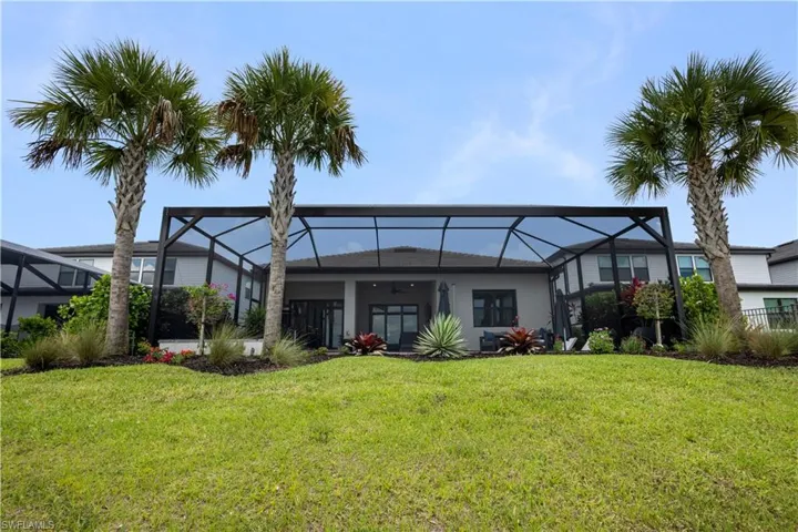 Expansive backyard featuring a manicured lawn, mature palm trees, and a screened-in lanai with a dark frame