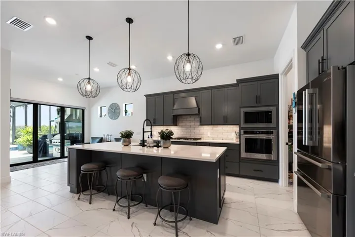Spacious kitchen featuring an expansive center island with seating, dark wood-finish cabinetry, a white tile backsplash, and stainless steel appliances