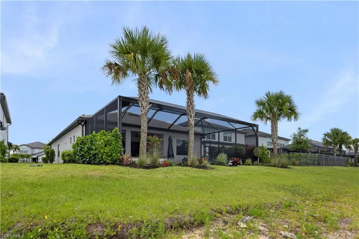 Expansive backyard featuring a screened-in lanai, mature palm trees, established landscaping, a manicured lawn, and a privacy fence