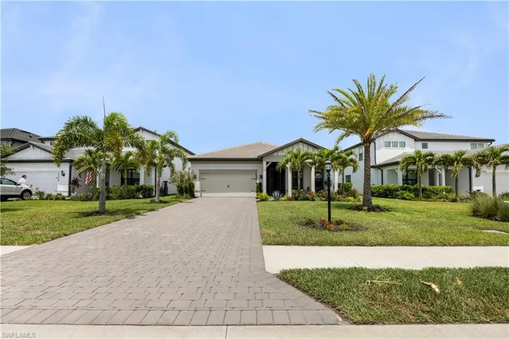 Contemporary single-story residence with a paver driveway, manicured lawn, multiple palm trees, and a two-car garage