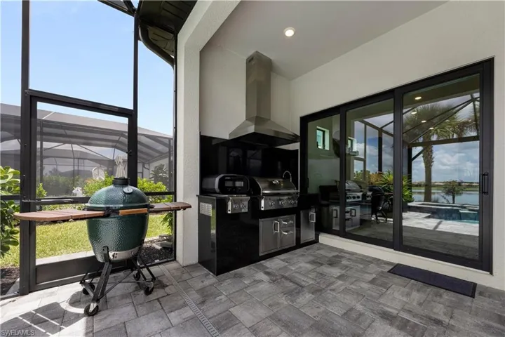 Screened outdoor kitchen featuring a built-in stainless steel grill, integrated range hood, under-counter storage, dark countertops, and dark tile backsplash