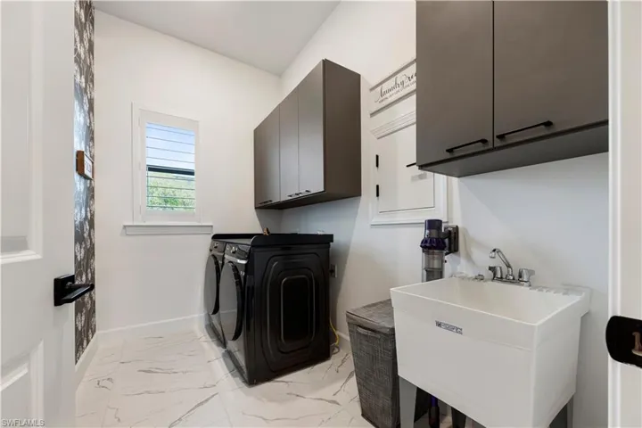 Dedicated laundry area featuring modern appliances, white marble-look tile flooring, and dark cabinetry