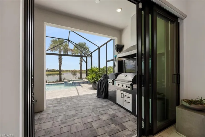 Outdoor living area featuring a screened enclosure, paver flooring, integrated outdoor kitchen with grill, pool, and spa