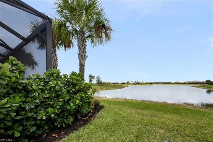 Expansive outdoor area featuring a screened enclosure, a manicured lawn, mature palm trees, a well-maintained shrub border with mulch, and a large freshwater lake