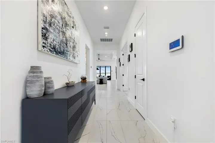 Bright hallway featuring large format tile flooring, recessed ceiling lighting, crisp white walls, and white interior doors with dark hardware