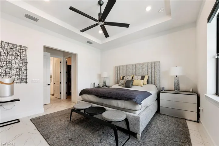 Recessed ceiling with a black ceiling fan, white walls, and light-toned tile flooring