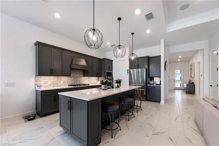 Contemporary kitchen featuring dark cabinetry, a large center island with seating, a light-toned countertop, and a light-colored tile backsplash