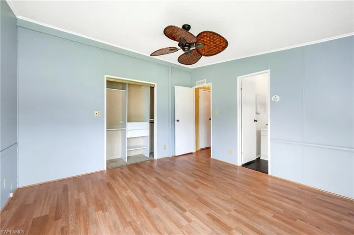 Unfurnished bedroom featuring ornamental molding, wood finished floors, a decorative wall, a ceiling fan, and a closet