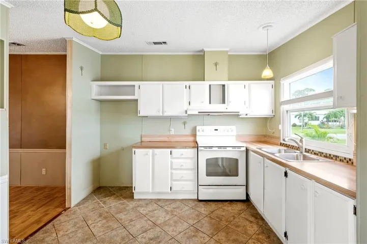 Kitchen with white cabinetry, white range with electric cooktop, ornamental molding, a textured ceiling, and light countertops