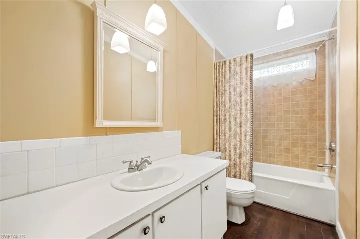 Full bath featuring shower / tub combo, vanity, dark wood-style flooring, ornamental molding, and backsplash