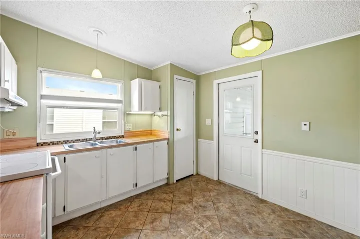 Kitchen featuring white cabinets, light countertops, a textured ceiling, a wainscoted wall, and ornamental molding