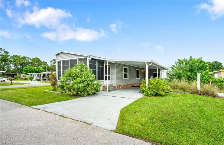 Manufactured / mobile home featuring a front yard, concrete driveway, and a carport