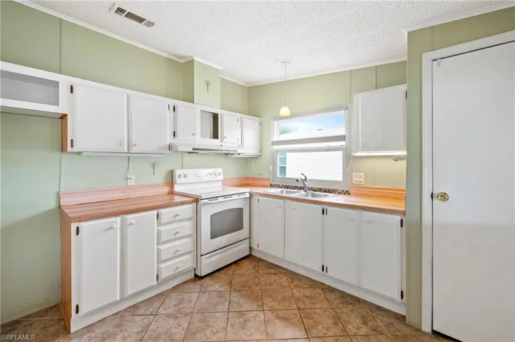 Kitchen featuring white cabinets, white electric stove, decorative light fixtures, ornamental molding, and a textured ceiling