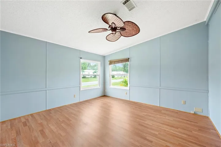 Unfurnished room featuring a textured ceiling, wood finished floors, a decorative wall, lofted ceiling, and ceiling fan