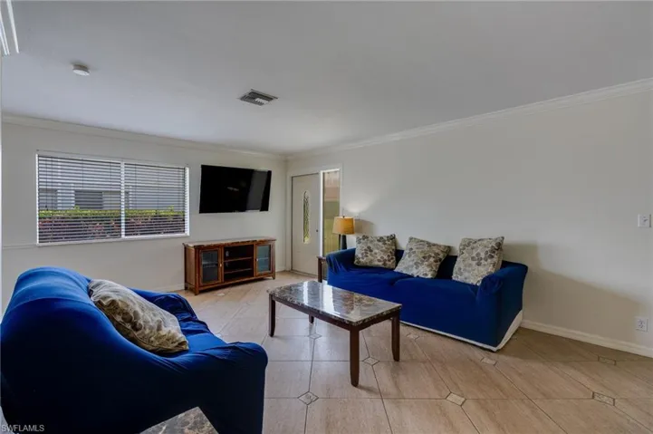 Open concept living area with light-toned tile flooring, white walls, and crown molding