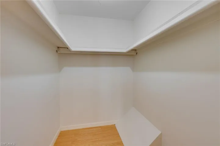 Walk-in closet featuring light wood-finish flooring, white baseboards, and a built-in shelf system
