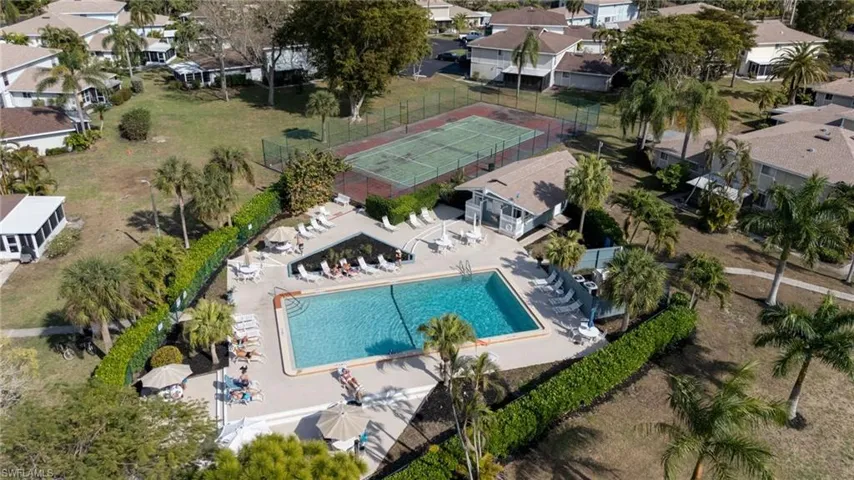 Community pool area with a rectangular swimming pool, surrounding lounge seating, and umbrella-covered tables