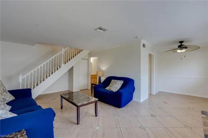 Open-concept living space with tile flooring, a staircase with white banisters, a black ceiling fan with integrated lighting, and crown molding