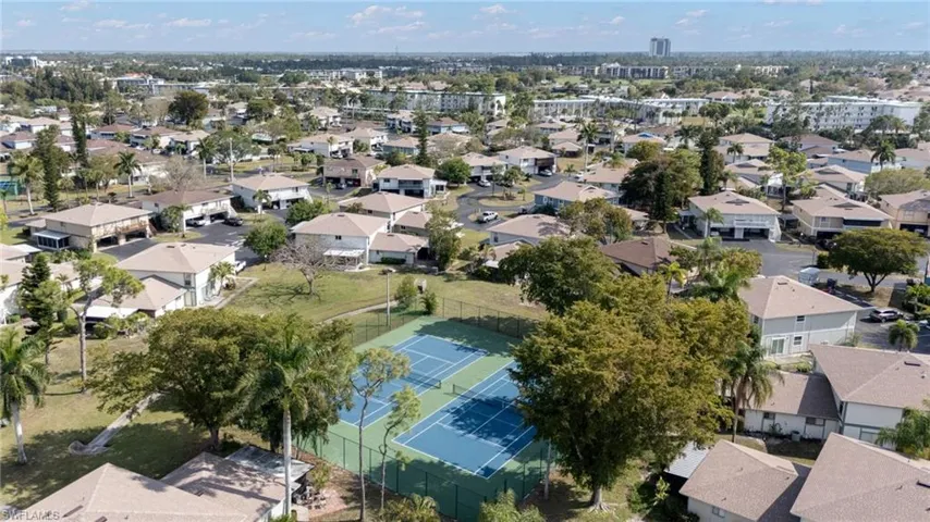 Neighborhood overview featuring a community tennis court with blue surfacing, surrounded by lush trees and mature landscaping