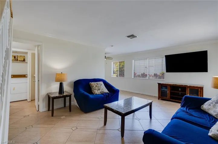 Living area featuring patterned tile flooring, a wall-mounted display, and horizontal window blinds