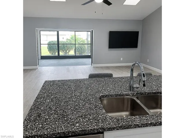 Kitchen featuring dark stone counters, a ceiling fan, light wood-type flooring, open floor plan, and a skylight