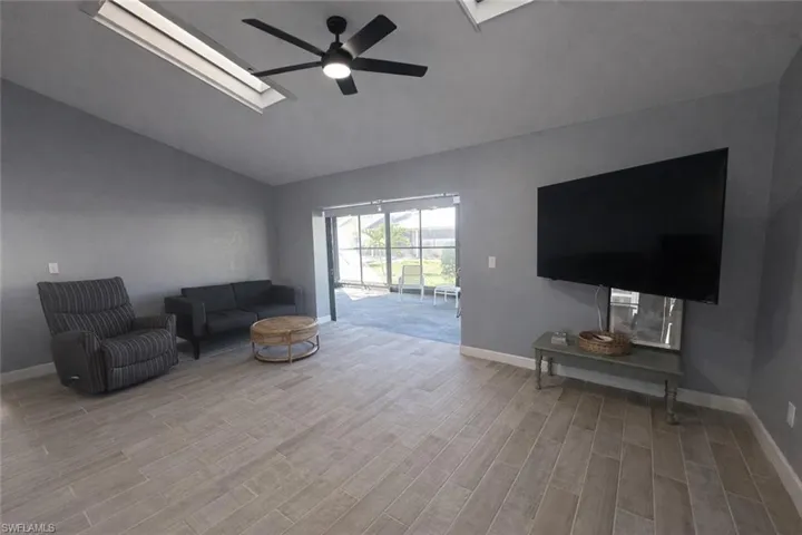 Living area with vaulted ceiling, wood finish floors, a skylight, and ceiling fan