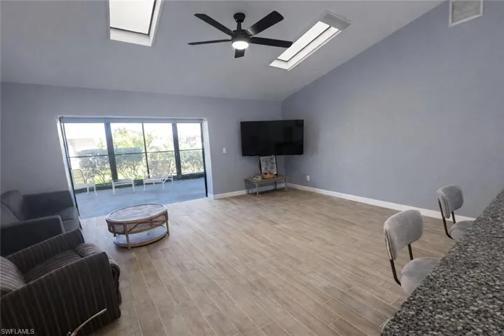 Living area with a skylight, light wood-style floors, a ceiling fan, and vaulted ceiling