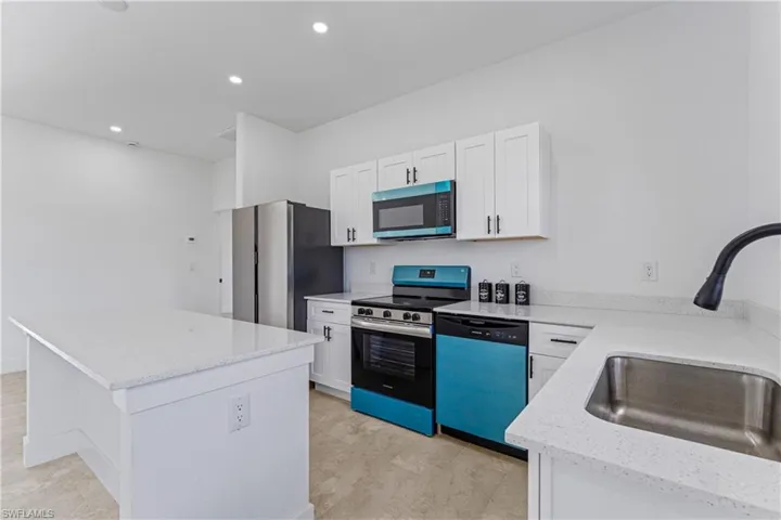 Kitchen with appliances with stainless steel finishes, white cabinetry, a kitchen island, recessed lighting, and light stone counters