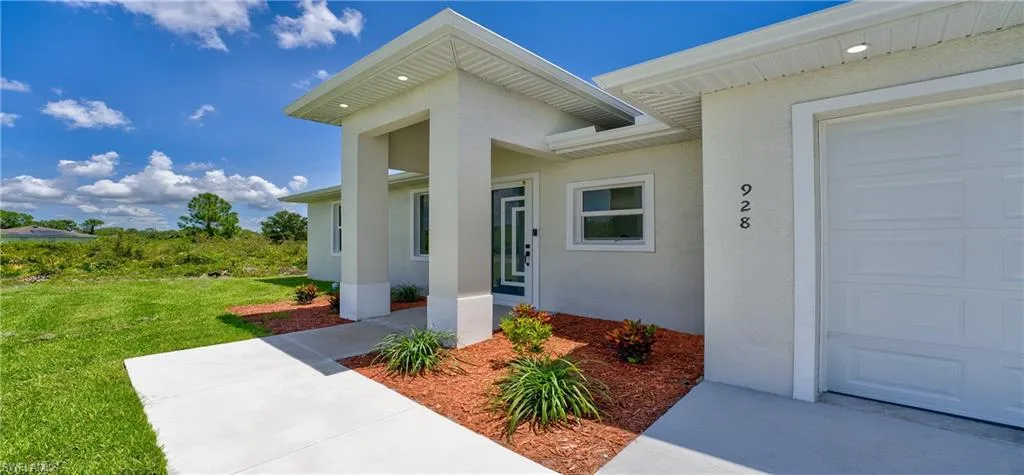 View of exterior entry featuring stucco siding, a garage, and a lawn