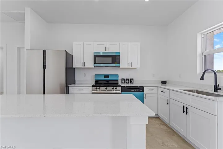 Kitchen with white cabinetry, appliances with stainless steel finishes, light stone countertops, and a center island