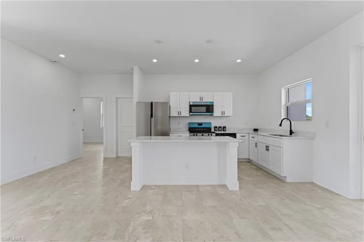 Kitchen featuring white cabinetry, stainless steel appliances, a center island, recessed lighting, and light stone counters