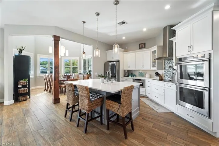 Kitchen with a kitchen island with sink, wall chimney exhaust hood, appliances with stainless steel finishes, dark wood-style floors, and a kitchen breakfast bar