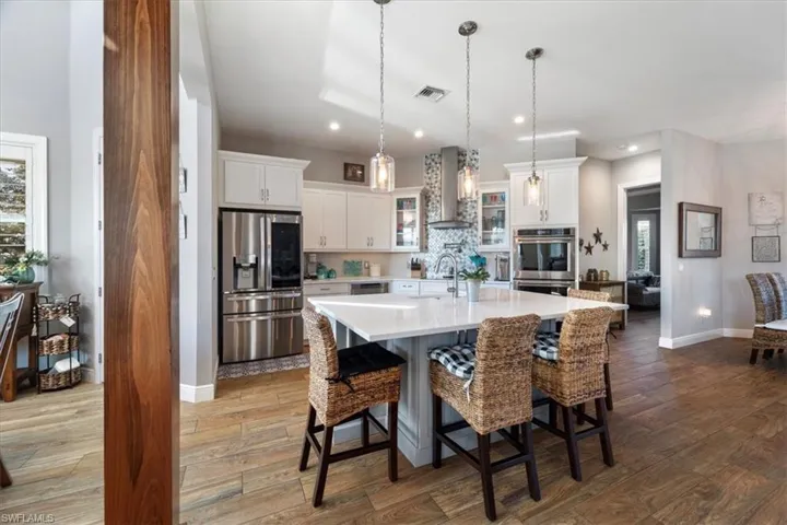 Kitchen featuring light countertops, wood finished floors, appliances with stainless steel finishes, wall chimney range hood, and visible vents