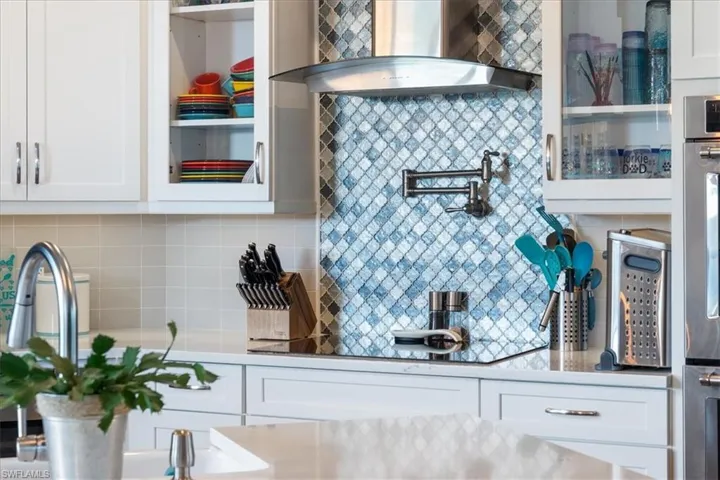 Kitchen featuring light countertops, tasteful backsplash, black electric stovetop, white cabinets, and wall chimney exhaust hood