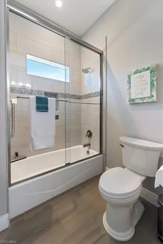 Full bath with baseboards, bath / shower combo with glass door, and toilet