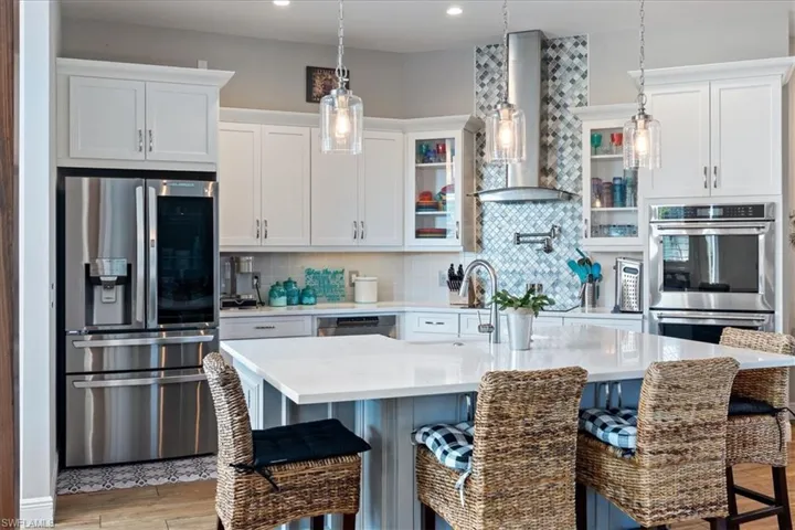 Kitchen featuring decorative backsplash, light countertops, wall chimney exhaust hood, appliances with stainless steel finishes, and a kitchen breakfast bar