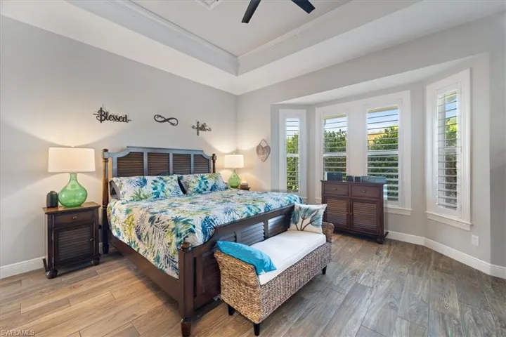 Bedroom featuring crown molding, a tray ceiling, baseboards, ceiling fan, and wood finished floors