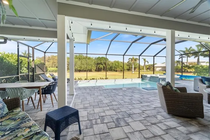 View of patio featuring glass enclosure and a pool with connected hot tub