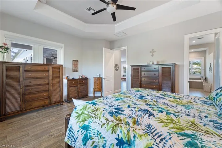 Bedroom featuring a raised ceiling, ornamental molding, wood finished floors, and visible vents